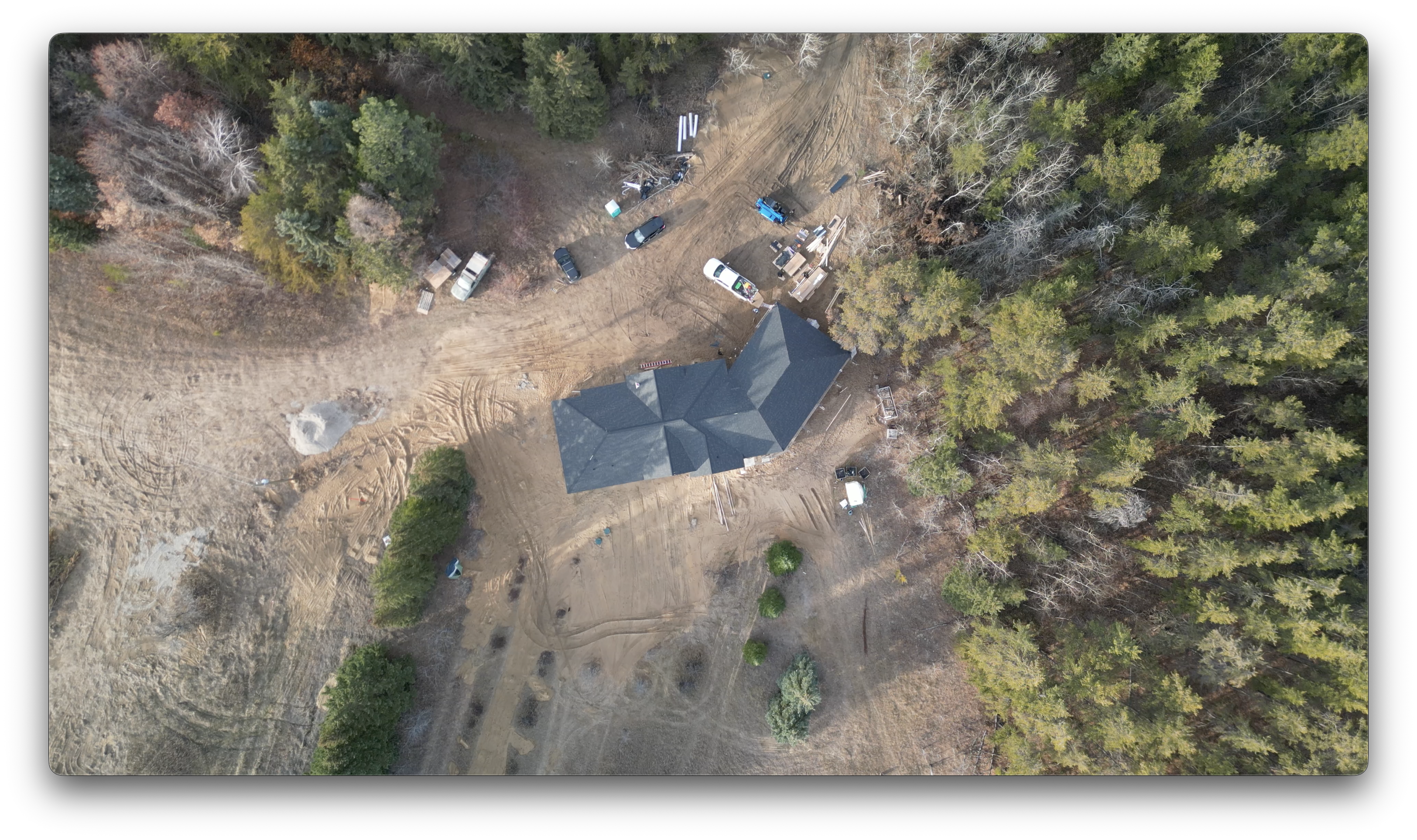 A high-altitude drone photo showing a newly built house with completed roofing surrounded by trees, construction vehicles, and building materials.