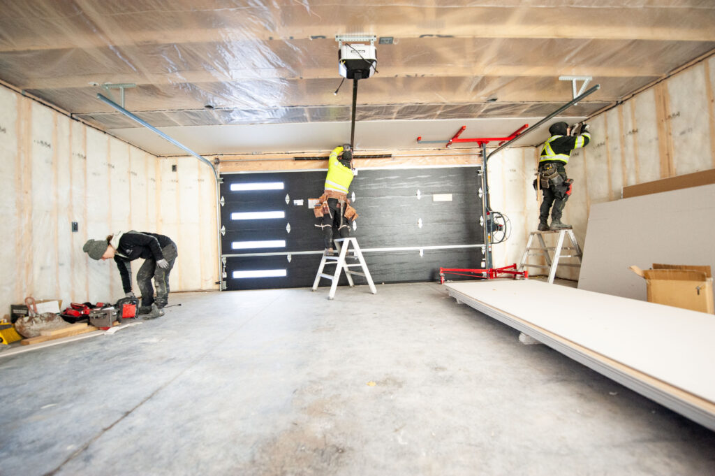 Crew installing ceiling drywall in a newly insulated 2-car garage with a 16x7 overhead door.