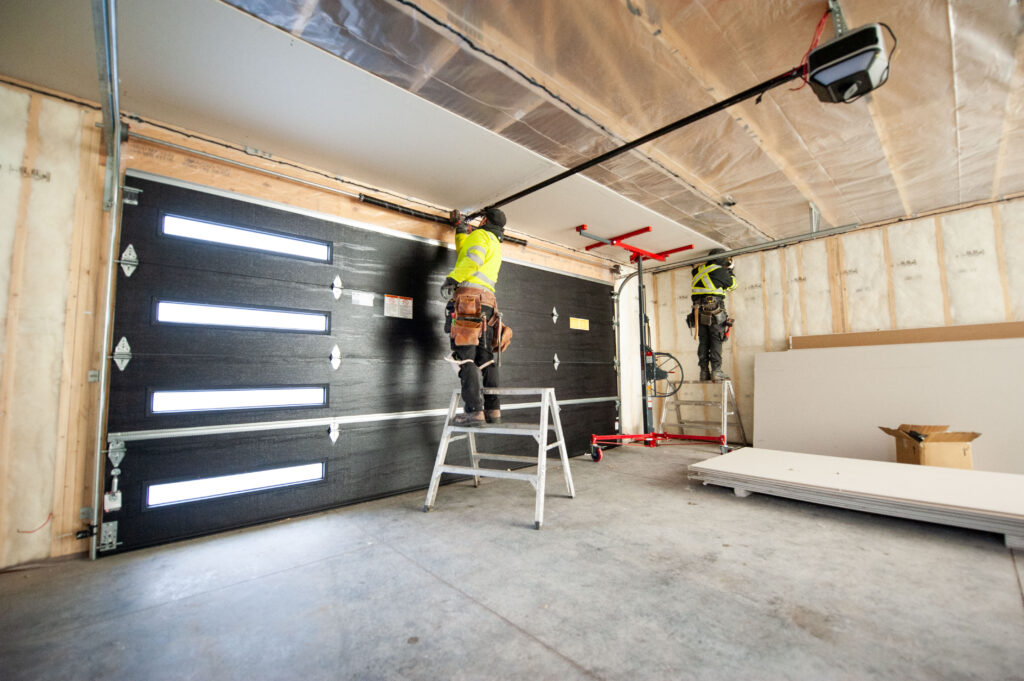 Installers lifting and securing ceiling drywall above a 16x7 garage door in a two-car garage.