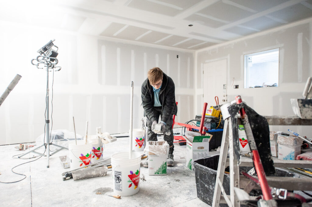 Worker mixing drywall mud inside a newly constructed garage with finished taping.