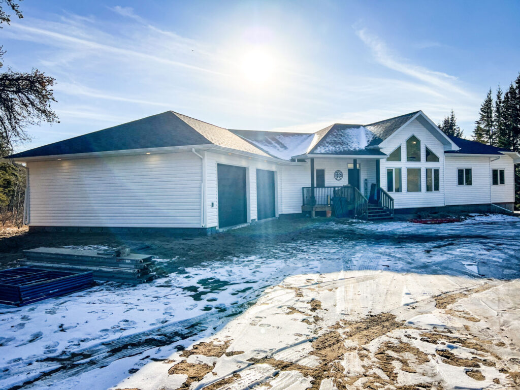 Finished attached garage on an acreage home in Alberta featuring white vinyl siding, asphalt shingle roof, and double overhead garage doors