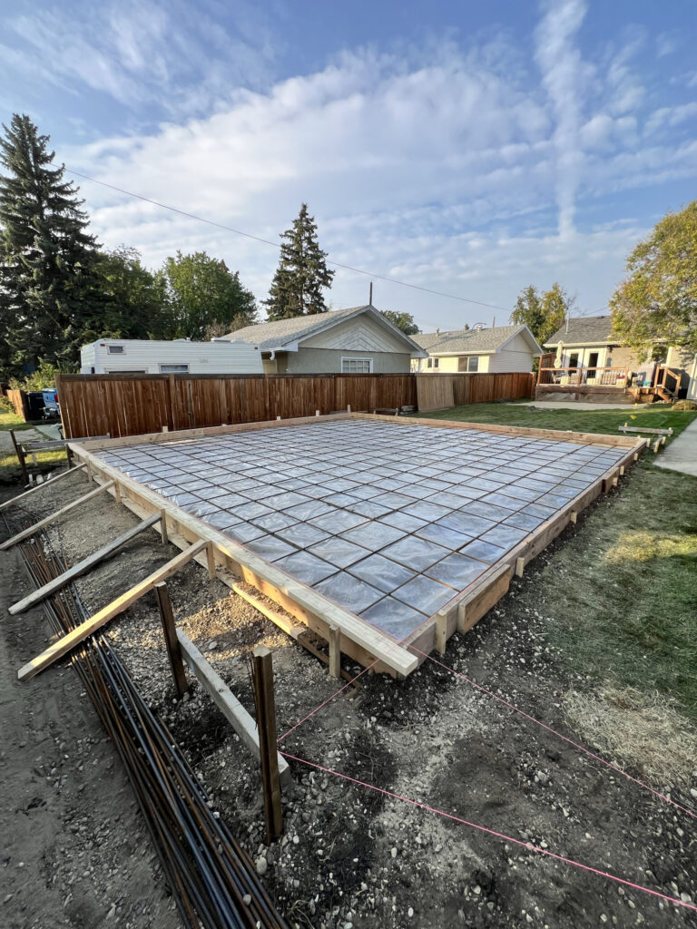 Detached garage concrete slab preparation in Edmonton showing rebar reinforcement, vapour barrier, and formwork by Alberta Builder Services