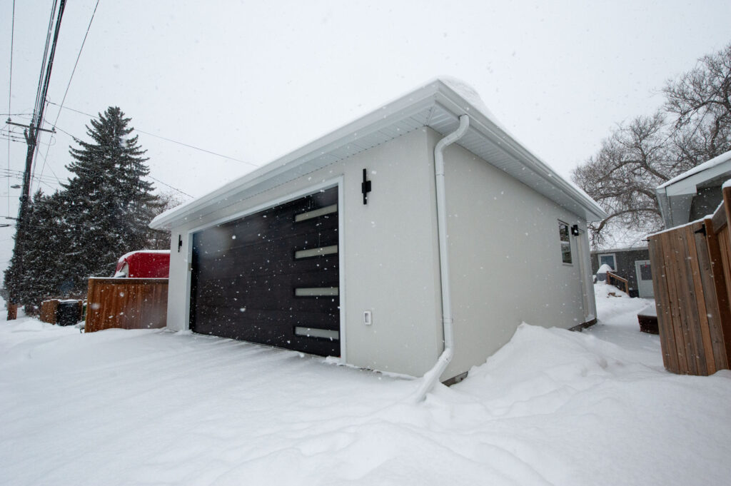 Finished detached garage in Edmonton with modern black overhead door, stucco exterior, soffit and eavestroughs built by Alberta Builder Services