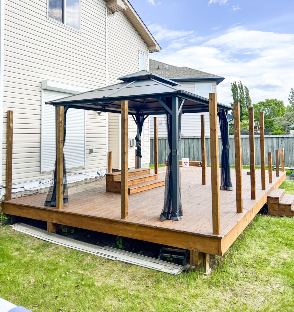 Newly built backyard deck in Edmonton featuring stained wood decking, installed posts, and a black metal gazebo with mesh panels.