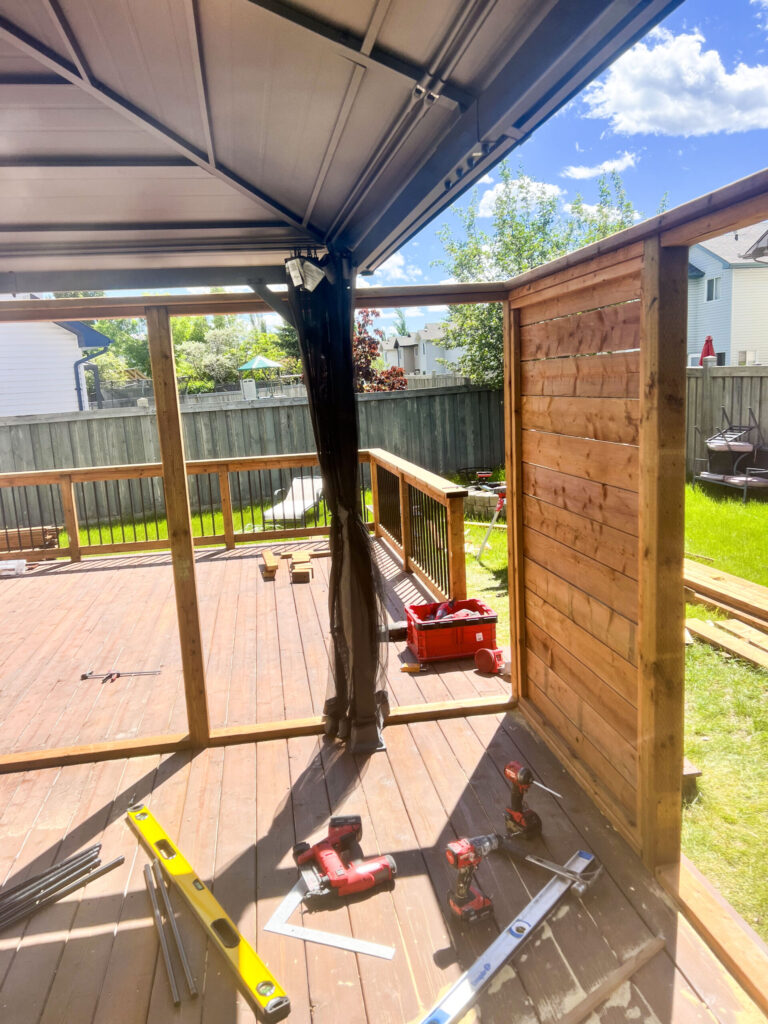 View from under gazebo showing deck construction progress in Edmonton, including the installation of a wooden privacy wall and railing sections.
