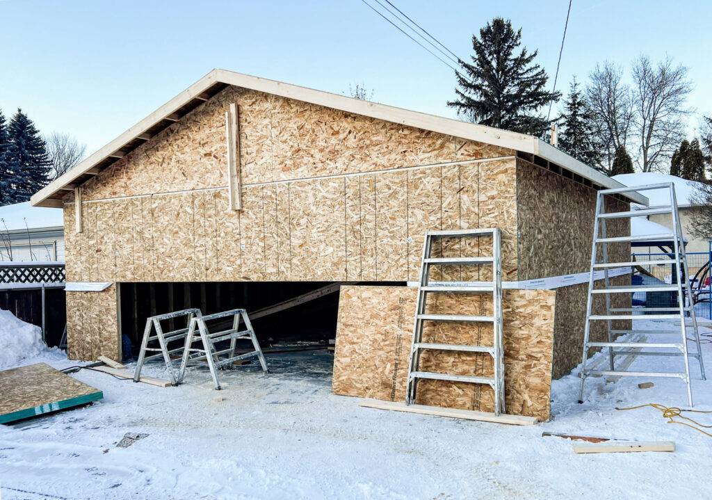 Detached garage exterior sheathing in Edmonton showing OSB walls, framed garage door opening, and roof overhangs by Alberta Builder Services
