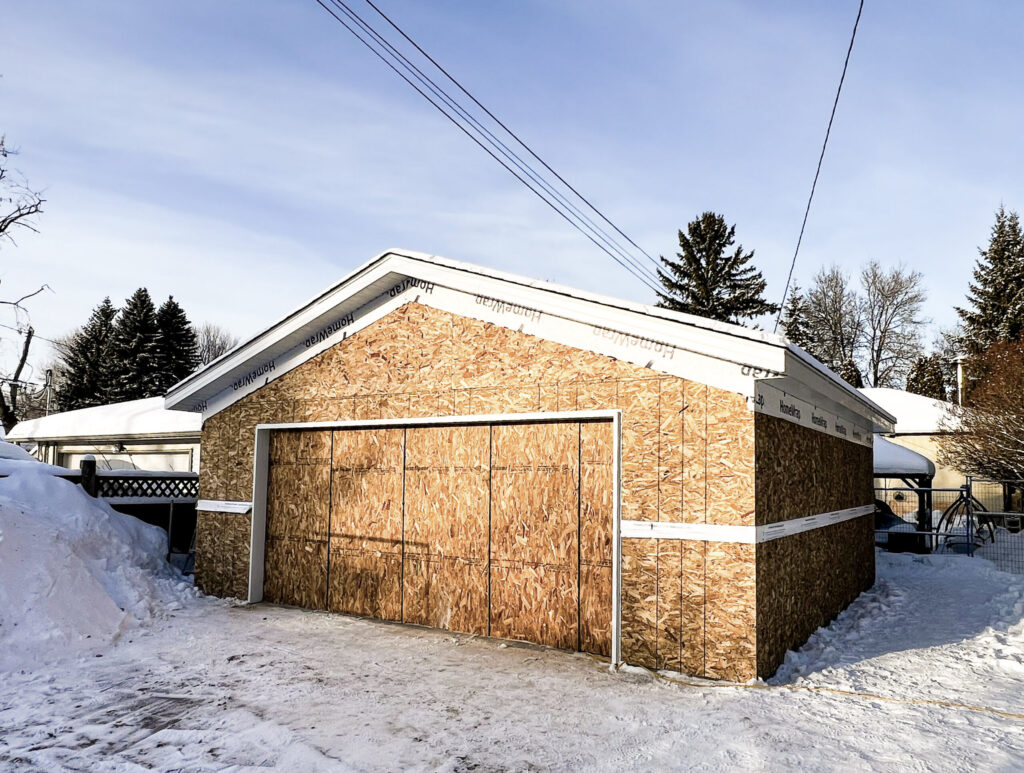 Detached garage in Edmonton fully framed and sheathed with roof underlayment and wrapped eaves, preparing for siding and exterior finishes by Alberta Builder Services