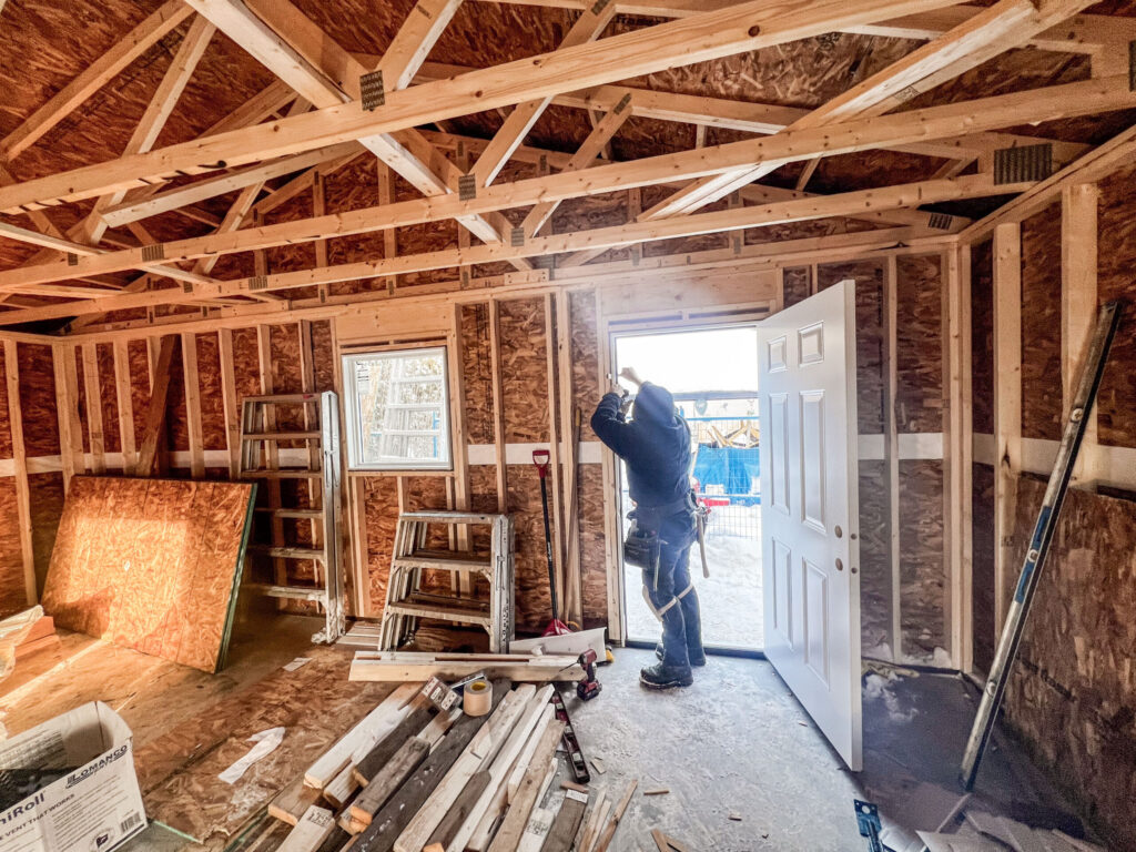 Interior of a detached garage in Edmonton showing completed framing, roof trusses, and installation of a man door by Alberta Builder Services