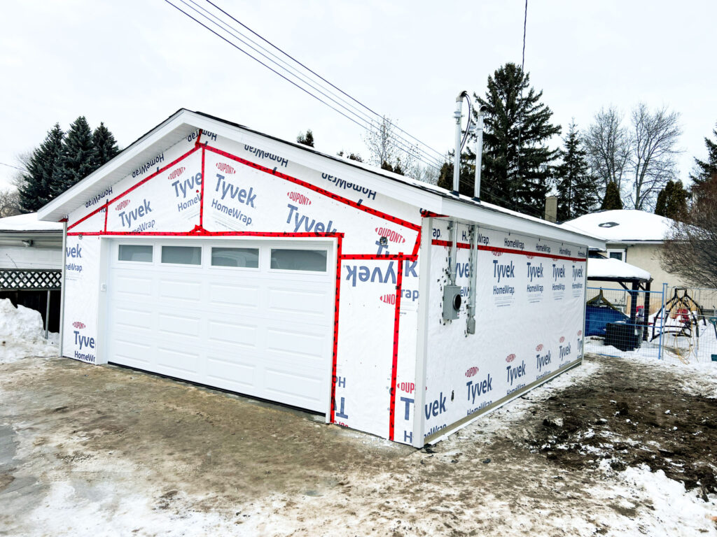 Detached garage in Edmonton with insulated overhead garage door installed and Tyvek housewrap applied, preparing for siding by Alberta Builder Services