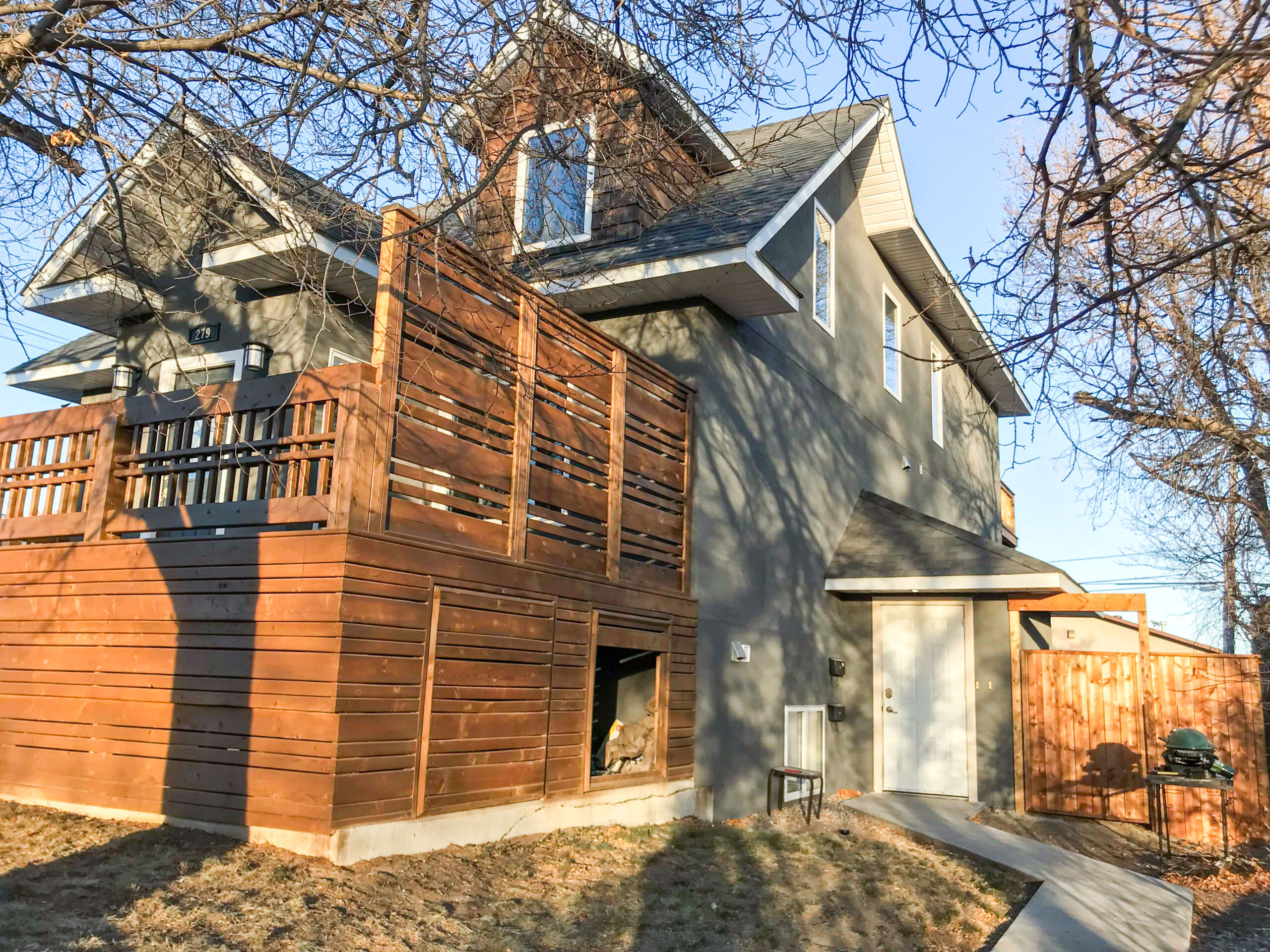A large wooden deck with privacy panels and built-in storage, attached to a modern home, built by Alberta Builder Services.