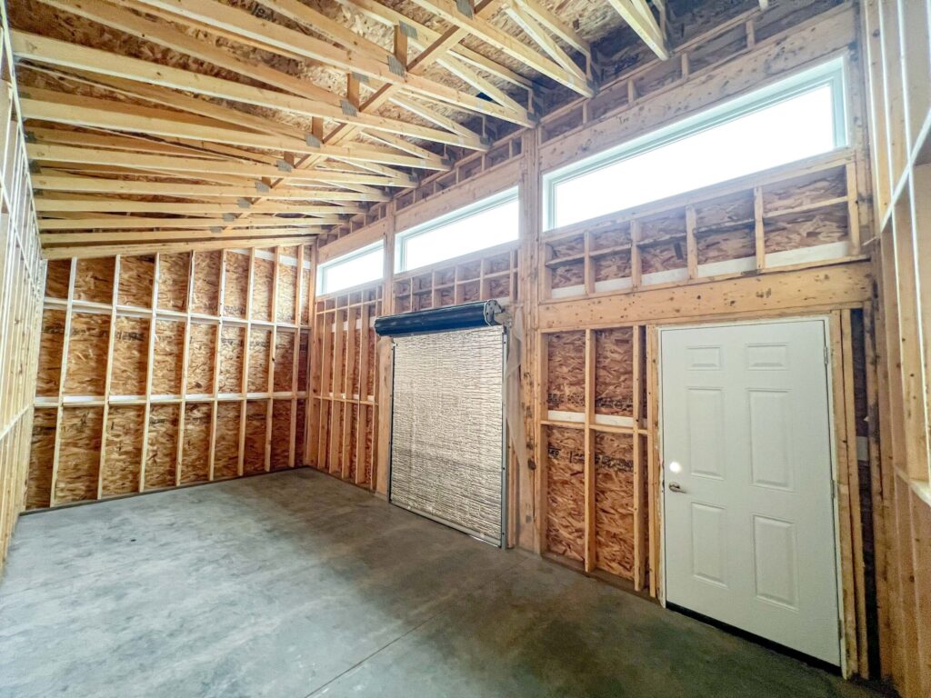 Interior of a custom oversized detached backyard shed with vaulted ceiling, transom windows, and overhead door opening in the Greater Edmonton area by Alberta Builder Services Ltd.